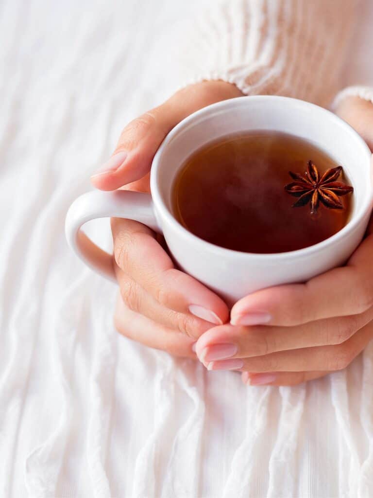 hands holding a cup of tea with star anise spice floating on top